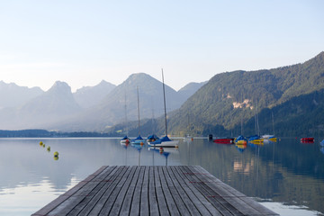 Empty wooden jetty on the lake shore with yachts and sailboats