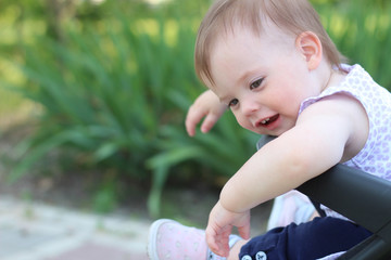 little, beautiful, smiling, cute redhead baby in a pram out-of-doors in a sleeveless shirt looking down