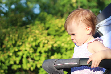 little, beautiful, smiling, cute redhead baby in a pram out-of-doors in a sleeveless shirt looking down