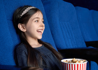 Little brunette watching comedy and laughing in cinema