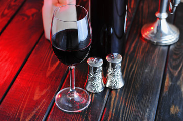 A glass of red wine with a bottle and a  candle on a wooden background.Candle light.