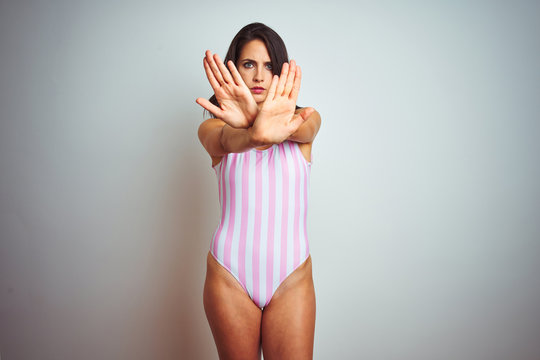 Young beautiful woman wearing striped pink swimsuit swimwear over isolated background Rejection expression crossing arms and palms doing negative sign, angry face
