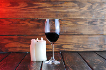 A glass of red wine with a bottle and a  candle on a wooden background.Candle light.