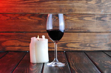 A glass of red wine with a bottle and a  candle on a wooden background.Candle light.