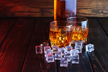 Two glasses of whiskey with ice cubes served on wooden planks.