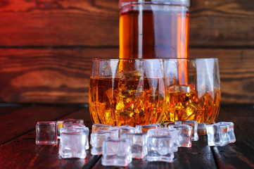 Two glasses of whiskey with ice cubes served on wooden planks.