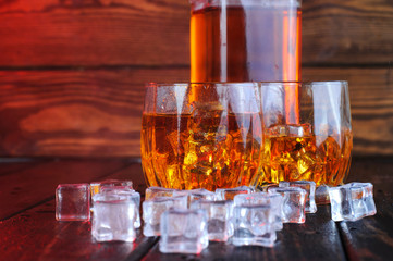 Two glasses of whiskey with ice cubes served on wooden planks.