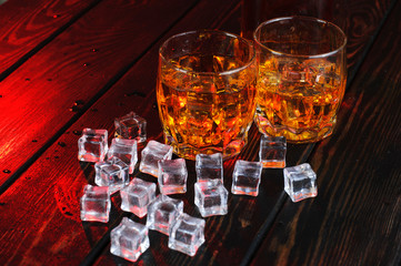 Two glasses of whiskey with ice cubes served on wooden planks.