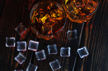 Two glasses of whiskey with ice cubes served on wooden planks.