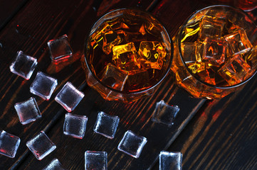 Two glasses of whiskey with ice cubes served on wooden planks.