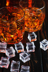 Two glasses of whiskey with ice cubes served on wooden planks.
