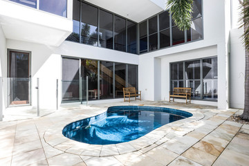 Big pool and wooden chairs. White walls and glass door.