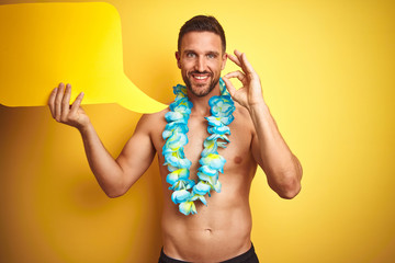 Handsome shirtless man wearing hawaiian lei holding speech bubble over yellow background doing ok...