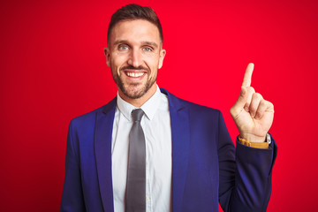 Young handsome business man over red isolated background with a big smile on face, pointing with hand and finger to the side looking at the camera.