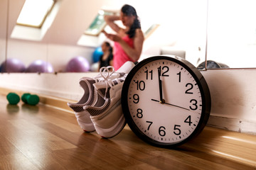 White sport shoes and clock in a gym. Group of active females squatting and stretching arms...