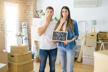 Fototapeta na wymiar Young beautiful couple holding blackboard with new home text at new house cover mouth with hand shocked with shame for mistake, expression of fear, scared in silence, secret concept