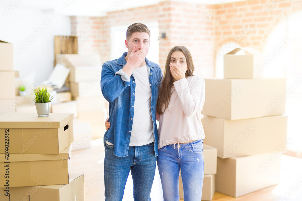 Canvas Prints Beautiful young couple moving to a new house shocked covering mouth with hands for mistake. Secret concept.