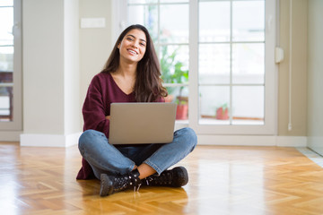 Young woman using computer laptop sitting on the floor happy face smiling with crossed arms looking...