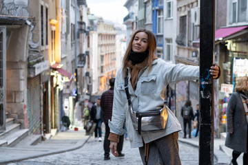 A young girl stands on the street of an old European city. Evening atmosphere, the lights are already included in the shops.