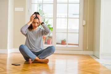 Young beautiful woman sitting on the floor at home suffering from headache desperate and stressed because pain and migraine. Hands on head.