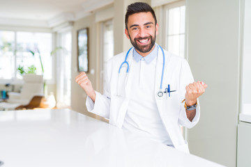 Handsome hispanic doctor man wearing stethoscope at the clinic celebrating surprised and amazed for success with arms raised and open eyes. Winner concept.