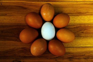 Top view of white egg in the middle of normal eggs on wooden table.