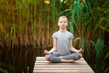 Little Girl meditating at sunrise on the beach near river