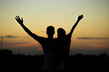 Fototapeta premium Silhouettes of father and daughter on his shoulders with hands up having fun, against sunset sky. Parenthood, family activities, beach holiday and vacation, support and love themes