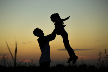 Silhouette of father throwing up his happy daughter in the air at sunset. family time togehter