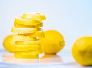 Fototapeta na wymiar Pile of juicy slices and whole lemons, close up view. Fruit composition on light background. Yellow lemons on white table. Blurred background. Selective soft focus