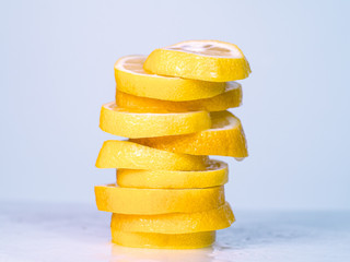 Fototapeta na wymiar Juicy lemon slices piled together on light table, close up view. Yellow lemon cutted into slices. Lemon juice dropping on table. Blurred background. Selective soft focus