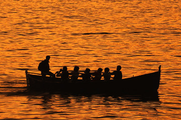Silhouette of rowboat and several rowers during sunset