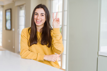 Beautiful young woman wearing yellow sweater smiling with happy face winking at the camera doing victory sign. Number two.