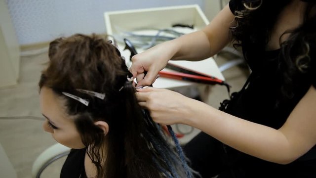 girl hairdresser weaves dreadlocks client in the salon