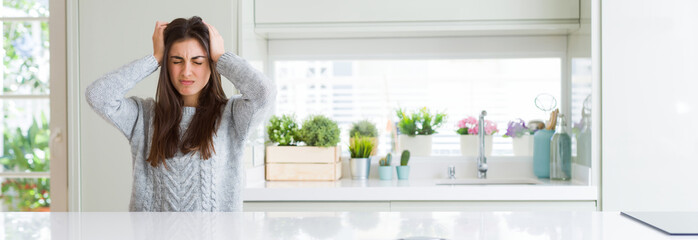 Wide angle picture of beautiful young woman sitting on white table at home suffering from headache...