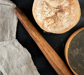 round baked bread and wooden old rolling pin on a black table