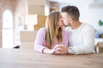 Young beautiful couple sitting on the table at home, hugging in love very happy for moving to new home with cardboard boxes behind them