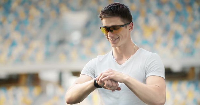 Happy handsome male checking data on smartwatch and smiling after successful workout.