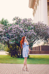Red-haired Model posing in the summer in a dress of blooming lilacs.