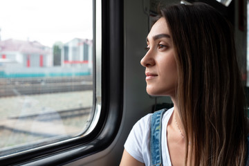Naklejka na ściany i meble A young girl on the train looking out the window. Good mood in the journey