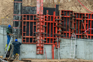 Builder working on construction foundation. Man in blue work clothes on the ladder brazing metal to...