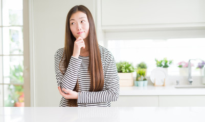 Beautiful Asian woman wearing stripes sweater with hand on chin thinking about question, pensive expression. Smiling with thoughtful face. Doubt concept.