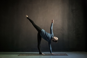 Young yogi woman practicing yoga in Half Moon exercise, Ardha Chandrasana pose. Indoor full length, black background