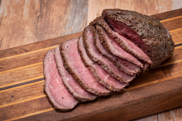 Sliced Grass Fed juicy Corn Roast Beef on natural wood cutting board.