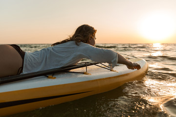 Beautiful young woman sitting on a stand up paddle board