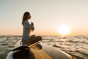 Beautiful young woman sitting on a stand up paddle board