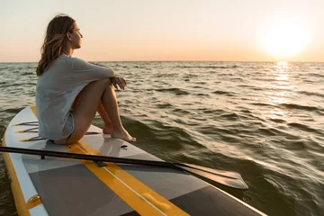 Fotobehang Beautiful young woman sitting on a stand up paddle board © Drobot Dean