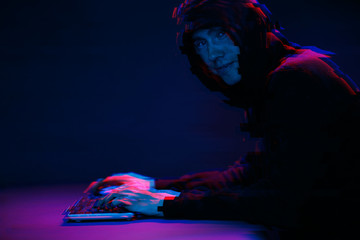 Hacker in the hood working with computer typing text in dark room. Image with glitch effect