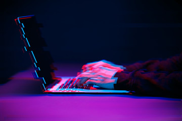 Hacker in the hood working with laptop typing text in dark room. Image with glitch effect