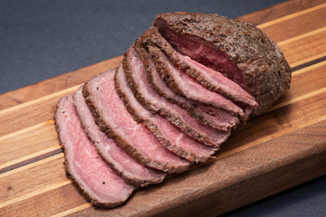Sliced Grass Fed juicy Corn Roast Beef on natural wood cutting board.